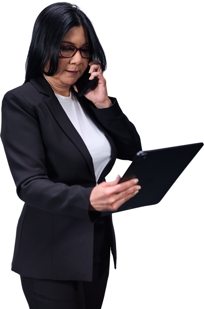 Una mujer que lleva una chaqueta negra está hablando por teléfono con alguien mientras mira la pantalla de una tableta.