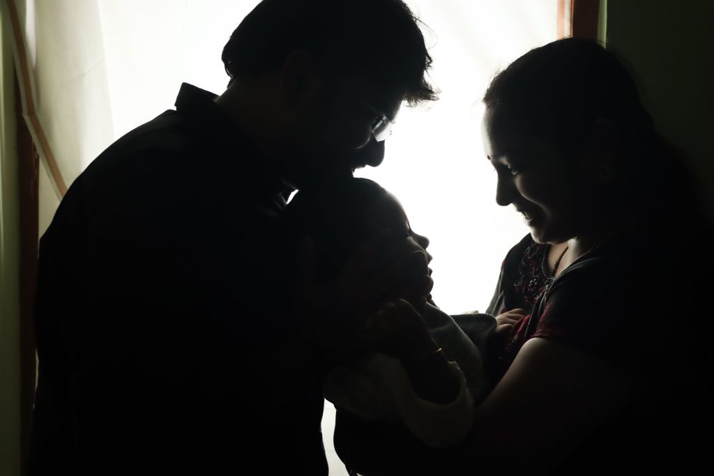 Silueta de unos padres que sostienen con cariño a su bebé en el interior de una casa, irradiando alegría y calidez.